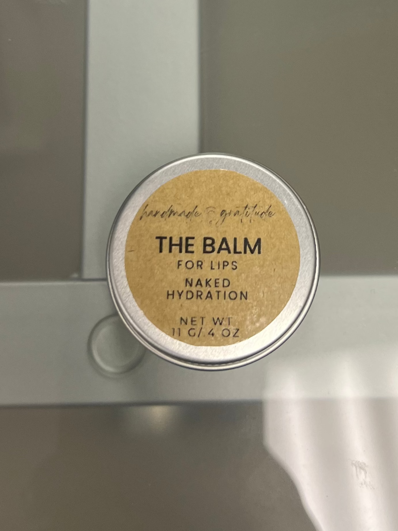 Small round container labeled 'The Balm' on a reflective surface